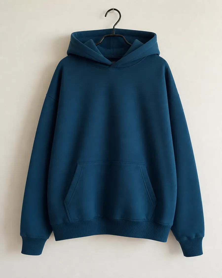 Foto original de la hoodie azul petróleo colgada de una percha, tomada contra una pared clara