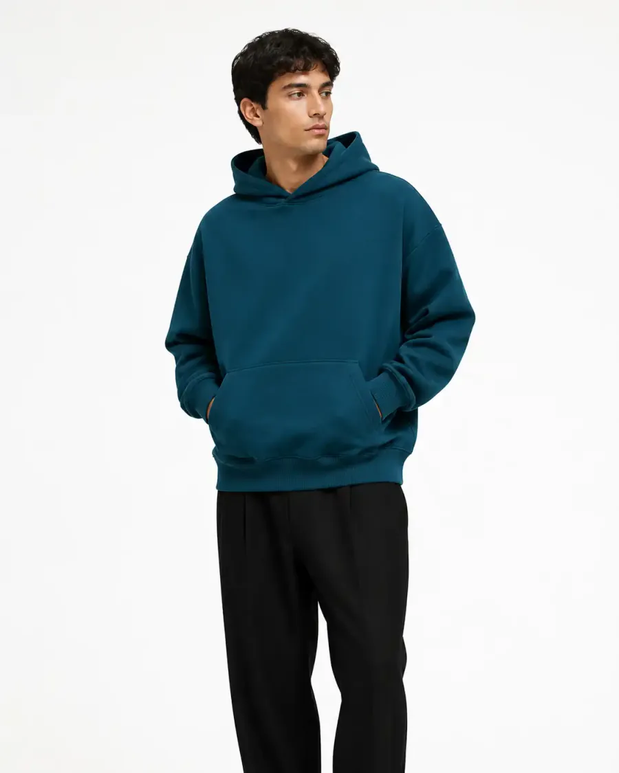 La misma hoodie azul petróleo puesta por un modelo en estudio, con pantalón negro y fondo blanco